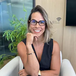 Retrato da advogada Dra. Elyssa Araújo, sorrindo de forma confiante com a mão apoiada no queixo, em seu escritório em Niterói. A imagem transmite a segurança e a autoridade de sua experiência institucional no direito do trabalho.