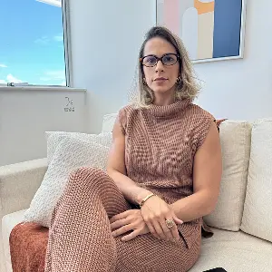 Retrato profissional da Dra. Elyssa Araújo, advogada especialista em direito do trabalho empresarial e compliance, sentada em seu escritório localizado em Niterói, Rio de Janeiro.